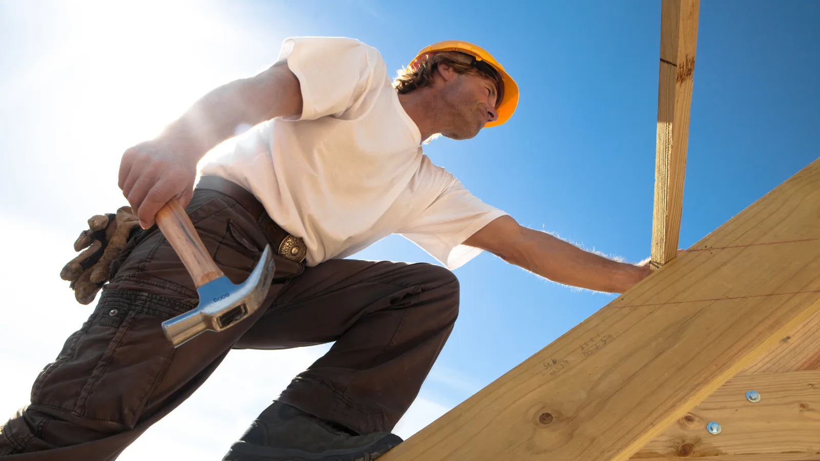 A roofer with a hammer climbing wooden roof framing